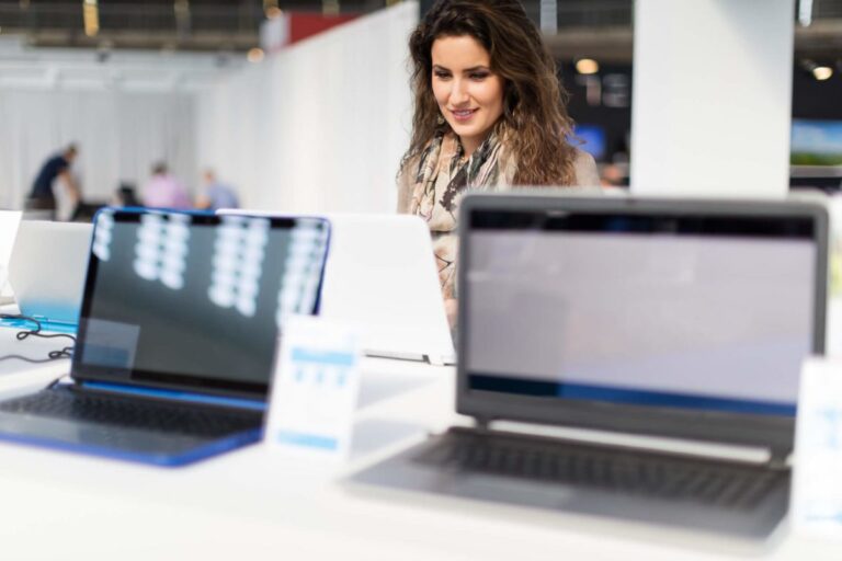 a imagem possui uma mulher sentada a mesa de um escritório com 3 notebooks