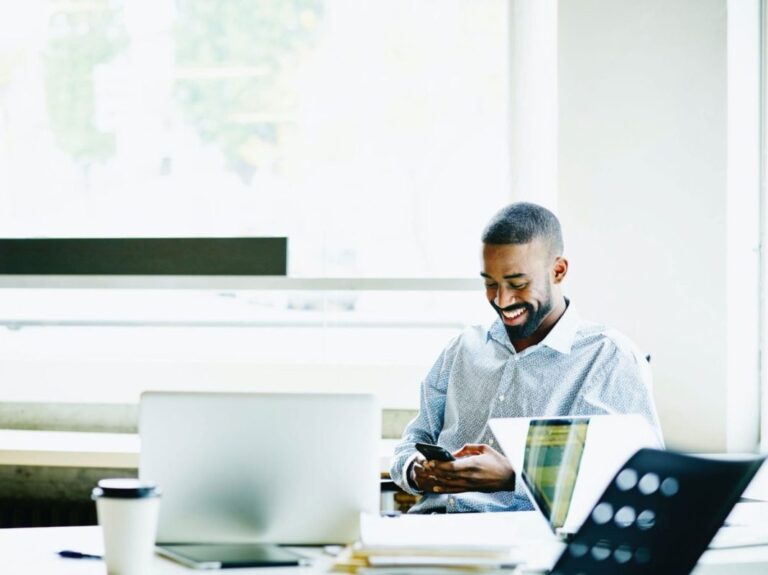 Homem negro em escritório, utilizando um aparelho celular